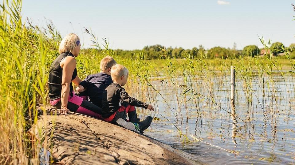 En vuxen person och två barn sitter på en klippa vid sjön och leker