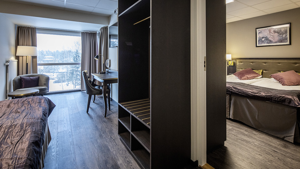 Bild på ett hotellrum med fåtölj, dubbelsäng och skrivbord med fin utsikt över staden  