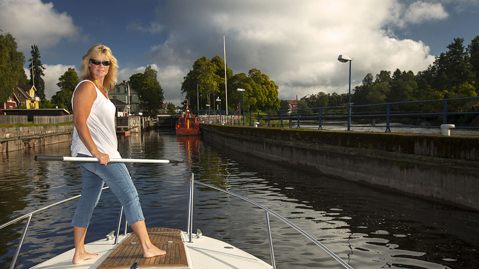 Sommar och sol. Båt på väg upp i Säffle kanal, på däck står en kvinna med båtshake för att vara redo inför  slussning. 