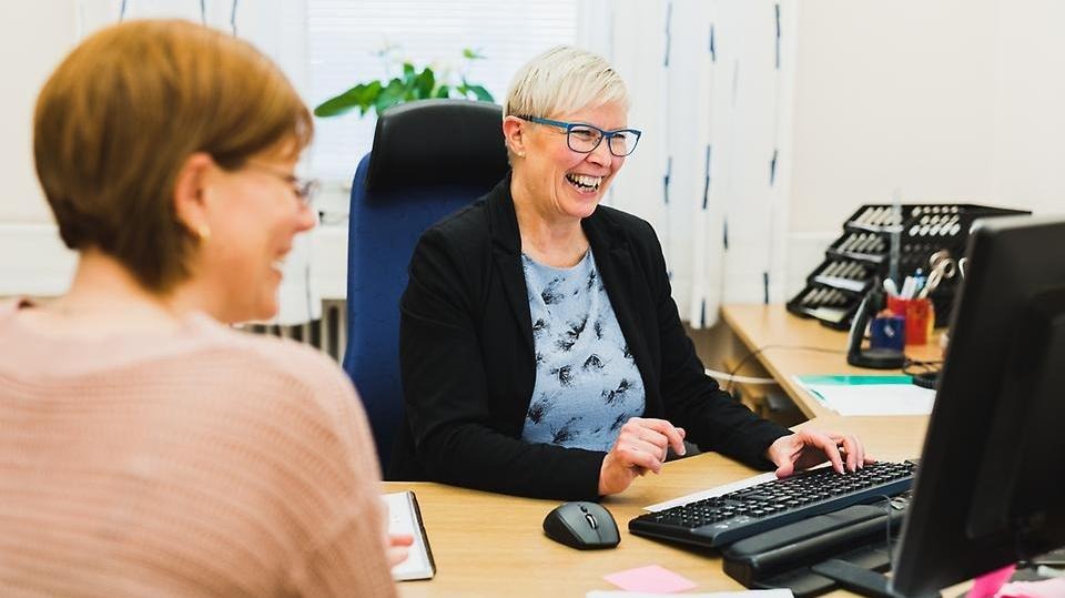 Två medarbetare i Säffle kommun skrattar tillsammans under ett möte vid en dator