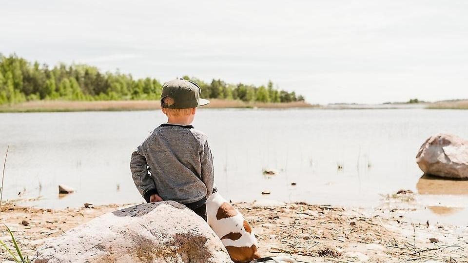 En liten pojke sitter på en sten vid stranden som ligger nära Restaurang Ekenäs.