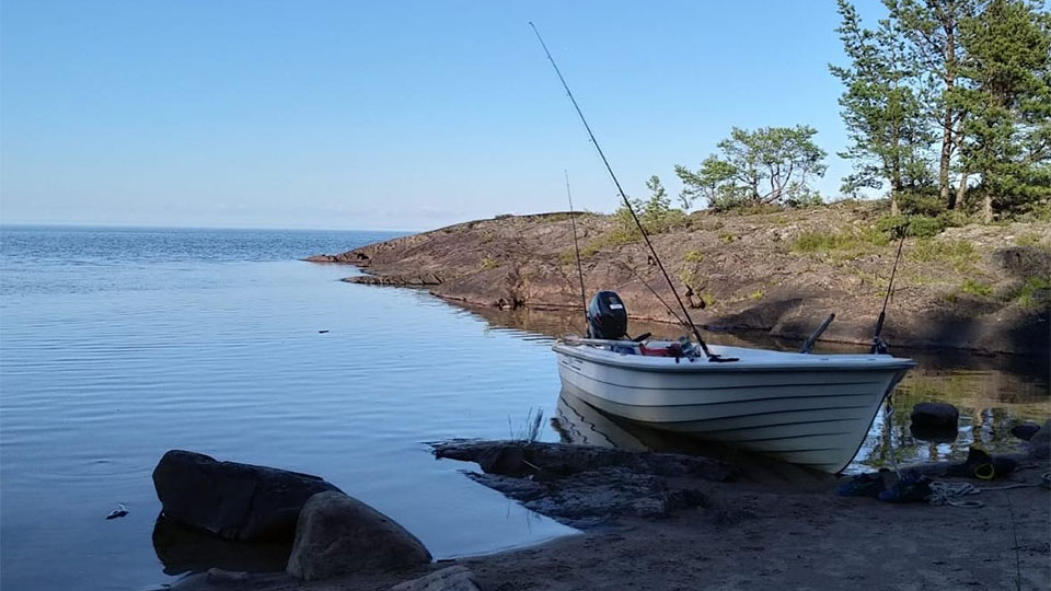 Här har fiskare tagit paus i en vik någonstans i Vänern. Båten har dragits upp på land, i bakgrunden breder Vänern ut sig, det syns inget inget land i sikte. 