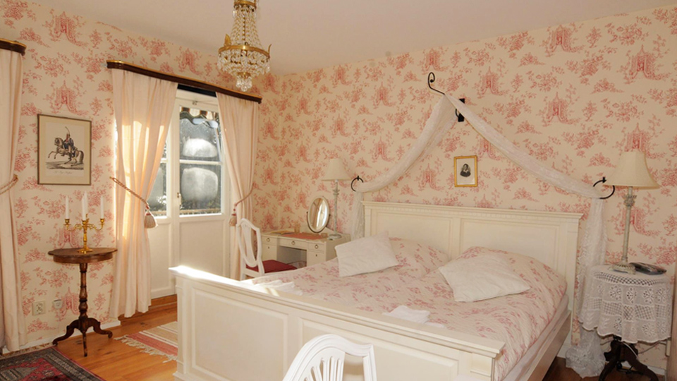 Ett vackert möblerat rum i färgerna vitt och rosa. I rummet finns en stor säng med sänghimmel 