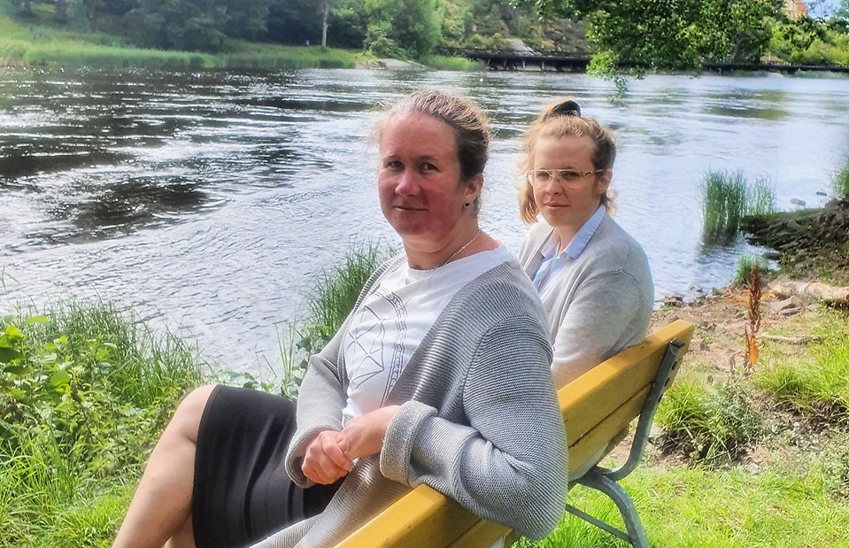 Funktionshinder- och anhörigkonsulenter Emma Kristensson och My Andersson sittande tillsammans på en bänk vid Byälven