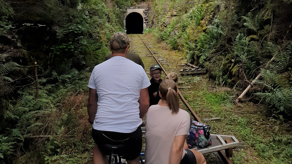 Upplev ett riktigt pirrigt äventyr, trampa dressin på den gamla järnvägen längs sjöar, i skog och genom tunnel. Familjen på bilden är på väg mot den 263 meter långa tunneln.