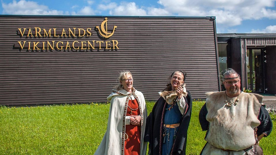 Här står den glada personal framför Vikingacentret. De är tidsenligt klädda, kvinnorna har klänningar i dova färger och mantlar, mannen har en lång väst på sig över tunika.